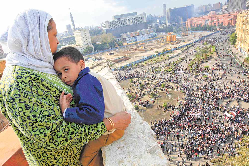 An Egyptian mother hugs her child as she watches some thousands of Egyptian protesters gather at Tahrir square in Cairo, Egypt, Sunday, Jan. 30, 2011, with the ruling National Democratic party building burned at top right behind the red coloured Egypt museum. The army sent hundreds more troops and armored vehicles onto the streets of Cairo and other cities but appeared to be taking little action against mass protests on Sunday. 