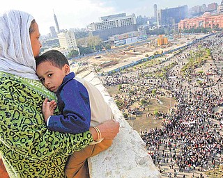 An Egyptian mother hugs her child as she watches some thousands of Egyptian protesters gather at Tahrir square in Cairo, Egypt, Sunday, Jan. 30, 2011, with the ruling National Democratic party building burned at top right behind the red coloured Egypt museum. The army sent hundreds more troops and armored vehicles onto the streets of Cairo and other cities but appeared to be taking little action against mass protests on Sunday. 
