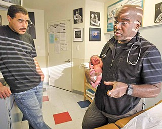 Pediatrician Dr. Gary Bean, right, talks with the parents of one-week-old twins, as he holds Samarah Newell, one of the twins, during their checkup in Oakland, California, January 14, 2011 as Emanuel Newell II, father of the twins, listens.