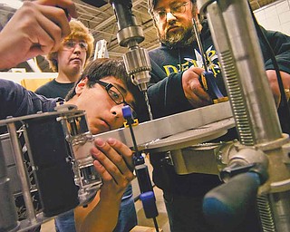 Fitch High School junior Paul O’Connor lines up a drill press to make holes for a mounting bracket in the control arm of the school’s robot. Assisting are club adviser Mike Gillman, right, and freshman Zack While.