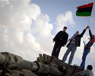 Libyan men celebrates on a destroyed tank belonging to the forces of Moammar Gadhafi in the outskirts of Benghazi, eastern Libya, Sunday, March 20, 2011. The tanks were destroyed earlier by U.S. and allied airstrikes.