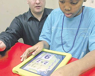 Curtis Bevly, a student at the Rich Center for Autism at Youngstown State University, uses an iPad while Brendan Considine, classroom supervisor at the center, watches. The center bought the devices using a federal grant. Officials say that because of their use of visual elements and their immediacy, iPads work well for children with autism.