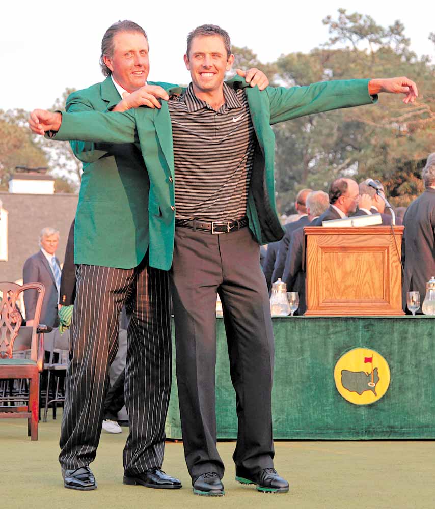 Former champion Phil Mickelson, back, helps Charl Schwartzel of South Africa with his green Masters jacket after winning the Masters golf tournament Sunday, April 10, 2011, in Augusta, Ga.  