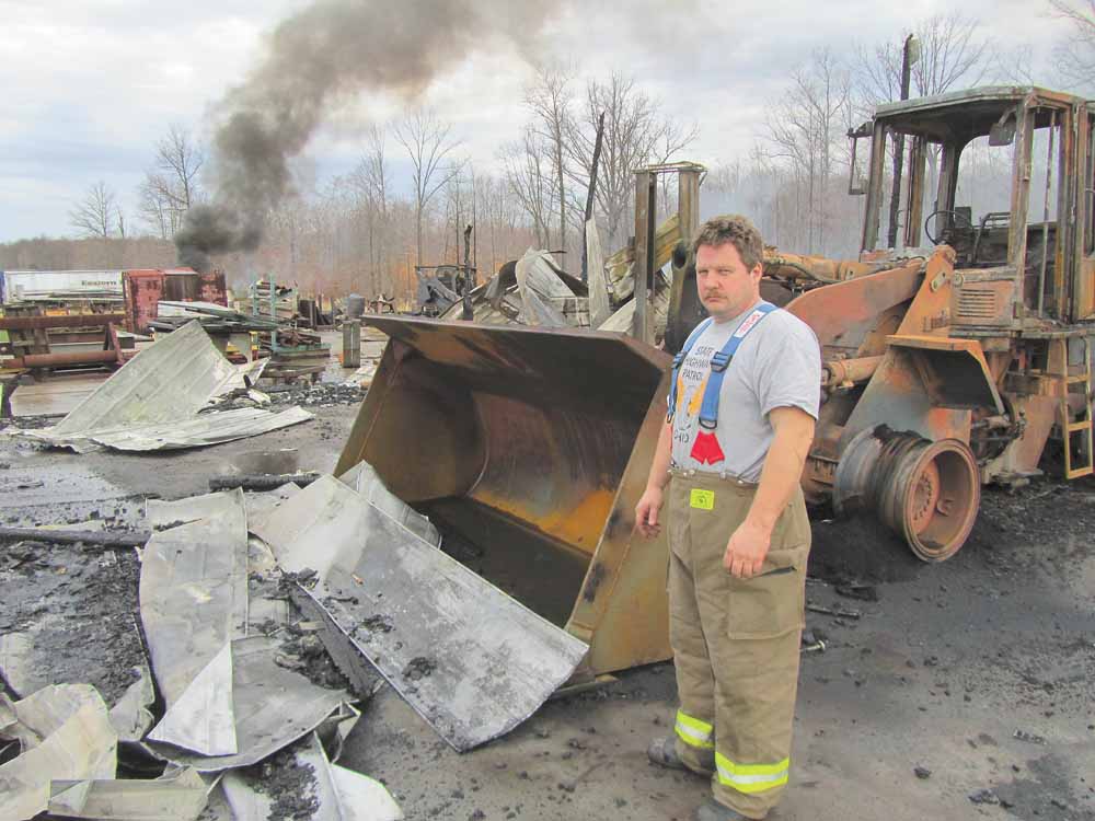 Todd Garland, Warren Township fi re chief, stands in front of one of two front loaders that were ruined at Doll Lumber, 1363 state Route 534 in Braceville Township, early Monday during a fire that destroyed a storage building and all of its contents.