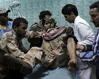 Medical staff and fellow rebels carry a Libyan rebel fighter who was injured during heavy fighting with pro-Gadhafi forces after being evacuated into the hospital of the recaptured town of Ajdabiya, Libya Monday, April 11, 2011. The Libyan rebel council rejected a cease-fire proposal presented by an African Union delegation because it did not provide for the departure of Libyan leader Moammar Gadhafi and his top associates.