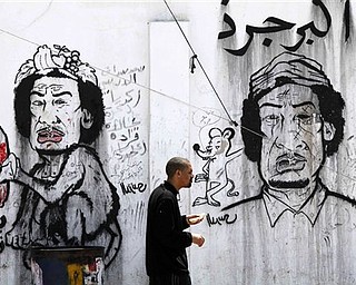 A man passes graffiti caricatures related to Moammar Gadhafi and Brega, during a funeral in Benghazi, Tuesday, April 19, 2011. The writing on the wall reads "the greatest rat of all," in Arabic. Europe is ready to send an armed force to Libya to ensure delivery of humanitarian aid and Britain said Tuesday it will dispatch senior military officers to advise the opposition  - signs that Western nations are inching closer to having troops on Libyan soil. 