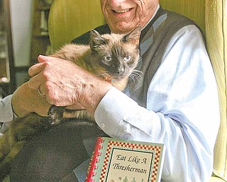 Hugh Earnhart holds his cat Boxcar Willie next to their cookbook “Eat Like a Thresherman,” a compilation of recipes from Earnhart’s grandmother. Willie “helped” Earnhart, a retired Youngstown State University professor, write the book.
