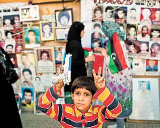 A boy holding a plastic weapon poses for a picture in front of portraits of people who were killed or have disappeared during Moammar Gadhafi's regime in Benghazi, Libya, Monday, May 16, 2011. Luis Moreno-Ocampo, prosecutor of the International Criminal Court in The Hague, announced Monday that he would seek arrest warrants against the leader of Libya, Moammar Gadhafi, his son Seif al-Islam and the country's intelligence chief on charges of crimes against humanity.