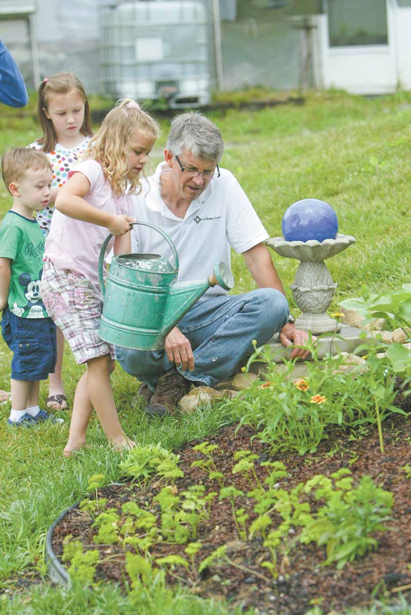 Greg Bowman, executive director of Goodness Grows, a faith-based food and farming ministry at Common Ground Church Community, watches as Julia Gregory, 7, waters plants. Also pictured are Jacob Bacvani, 3,and Leah Bacvani, 7.