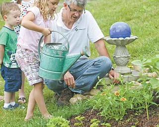 Greg Bowman, executive director of Goodness Grows, a faith-based food and farming ministry at Common Ground Church Community, watches as Julia Gregory, 7, waters plants. Also pictured are Jacob Bacvani, 3,and Leah Bacvani, 7.