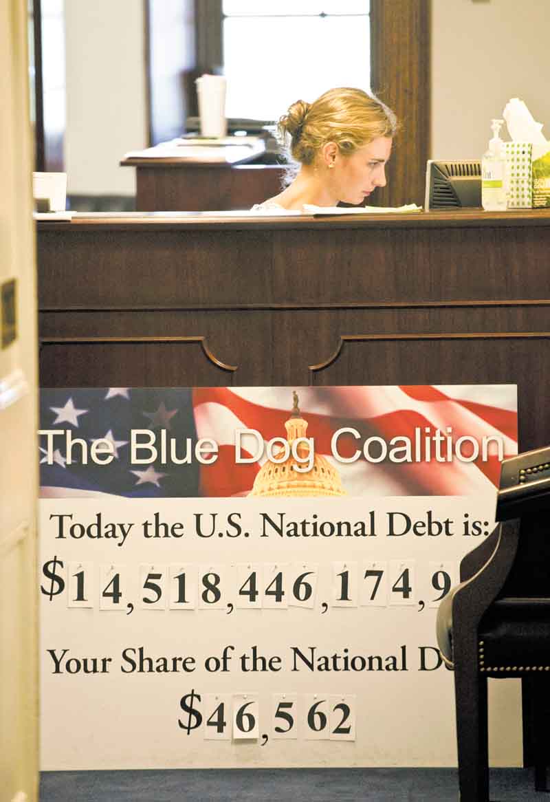 A staff member sits at a reception desk behind a national debt poster in the office of Rep. Jim Cooper, D-Tenn., Tuesday, July 26, 2011, in the Longworth House Office Building on Capitol Hill in Washington. (AP Photo/Harry Hamburg).