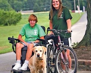 Jill Molnar, who has advanced multiple sclerosis, and her daughter, Megan Molnar, with Jill’s constant companion, Odie, a yellow labrador retriever, at the Molnar Farm Market in Springfield Township, where Jill runs the cash register. Megan, a second-year occupational therapy student at Duquesne University in Pittsburgh, is riding this weekend in the 150-mile Ohio Bike MS Pedal to the Point event as team captain of Jill’s Jaunters.