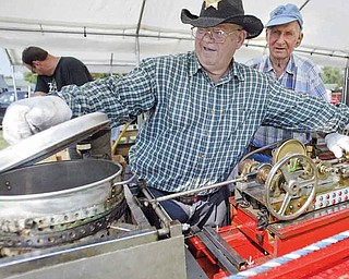 Thomas Hacon, left, of Austintown makes popcorn at his booth at the Canfield Fair. The octogenarian has been making popcorn at the fair for nearly 20 years. His machine is powered by compressed air and LP gas, patterned after a steam machine he saw when he was a boy. He gives samples away. At right, Richard Peters helps out.