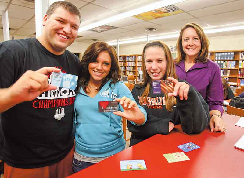 From left, Springfield High School senior Stephen Lyons, junior Shelby Romanchuk, senior Lexy Zubic and school librarian Amy Crowe show off the students’ new library cards. Students will use the public library instead of school computers to access academic databases — saving the district about $5,000 annually.