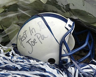 A miniature football helmet lies among flowers left at the foot of a statue of Joe Paterno outside Beaver Stadium on the Penn State University campus after learning of his death Sunday, Jan. 22, 2012 in State College,Pa.. (AP Photo/Gene J. Puskar)