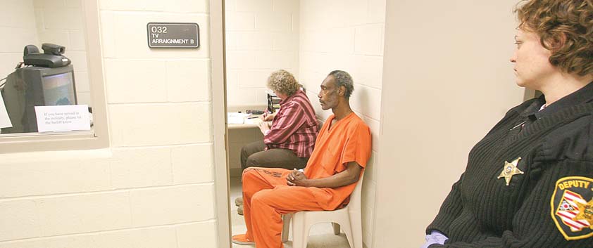 Mahoning County Deputy Sheriff Stephanie Harchar stands guard as Artis Walton is video-arraigned from the county jail on a criminal-trespass charge. Brenda Rider, sitting next to Walton, is a Youngstown Municipal Court bailiff who took notes. Walton, who pleaded innocent, was one of seven inmates to be video-arraigned Monday.
