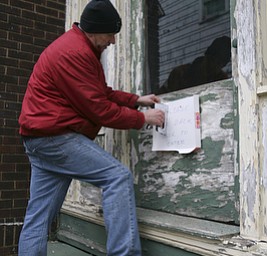 JESSICA M. KANALAS | THE VINDICATOR..Volunteer Bob Harrell of Youngstown puts a sign on a side door after replacing the glass window.