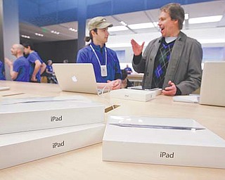 A customer talks with an Apple worker, in blue, at an Apple store on the first day of the launch of the new iPad, in San Francisco. A research firm that has taken apart a new iPad says it’s more expensive to make than the previous version was when it launched a year ago. The tablet’s retail price is the same, so that means Apple is making less from each sale. Since the first iPad, Apple has been pricing the tablet aggressively, making it hard for competitors to match its features for the same price.