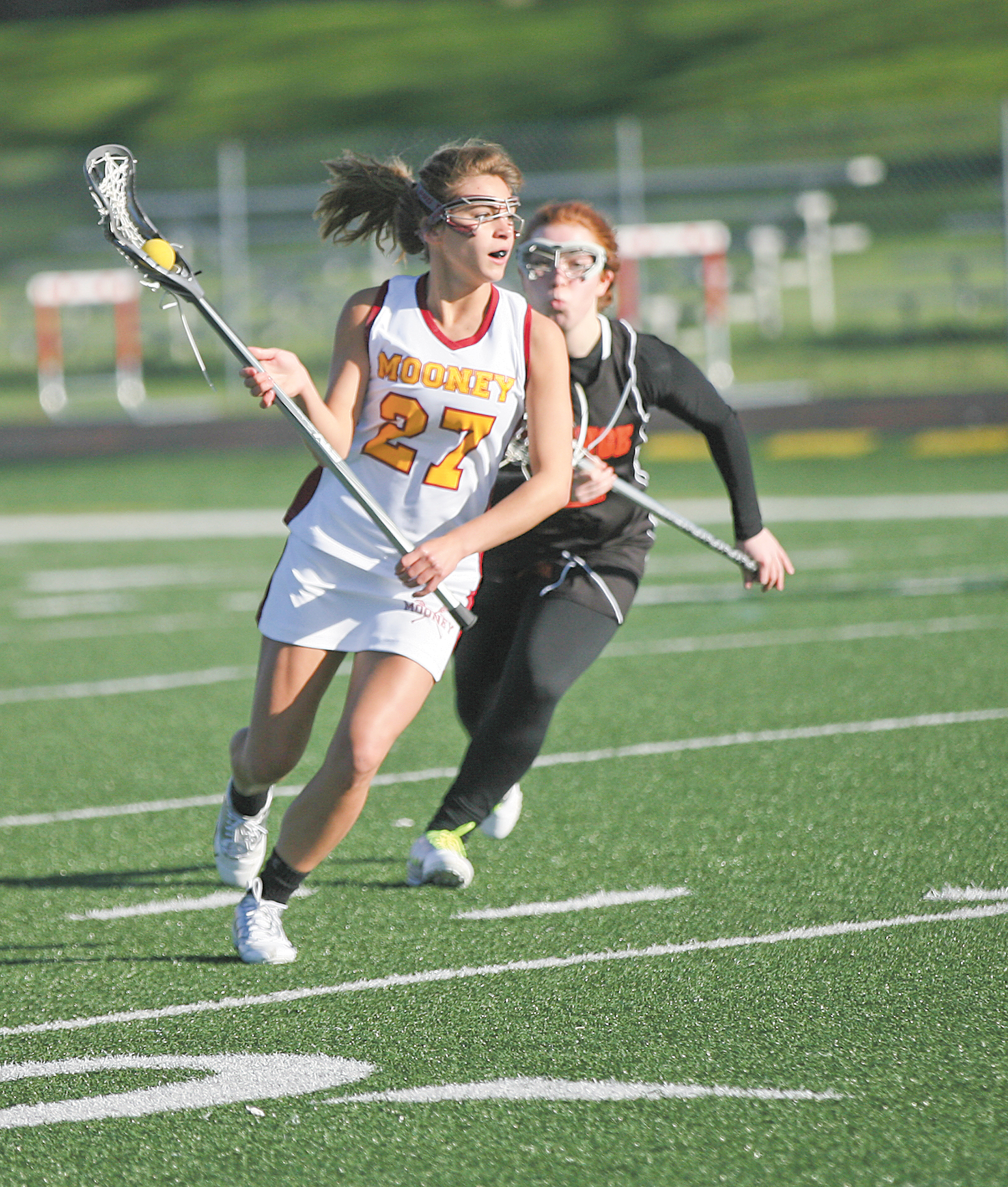 Cardinal Mooney’s Makenna Ozenghar, pursued by Orange defender Arianna Cerqueira, looks to pass during the first half of a lacrosse game Wednesday at Mooney High School. The Cardinals dominated the Lions, 16-0.