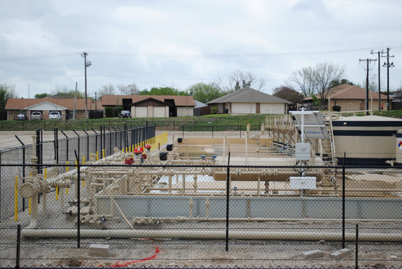 A drilling well pad sits in the foreground, just across the street from a regular neighborhood of Fort Worth, Texas. 