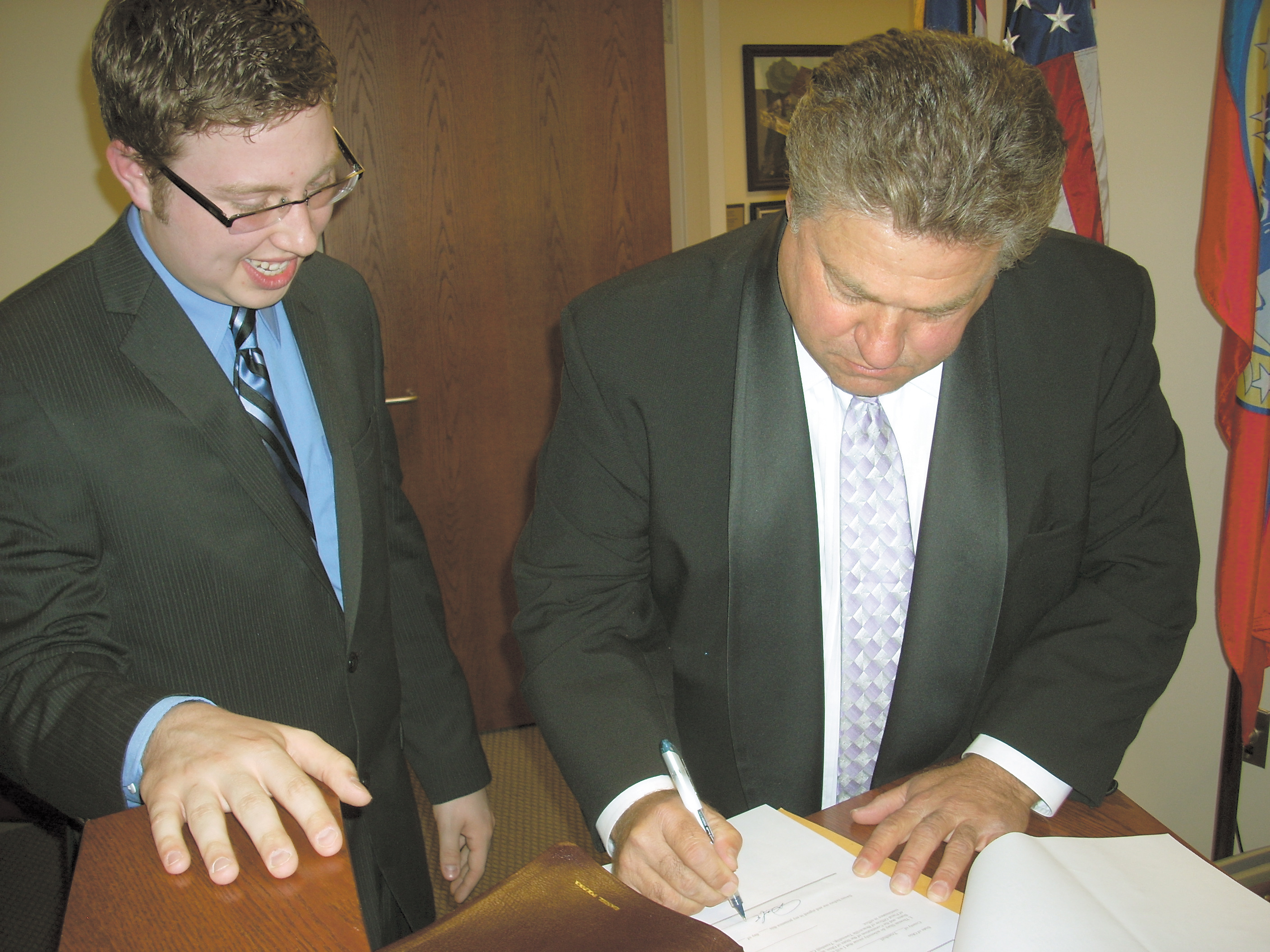 Tom Shay, left, 19, Braceville Township’s new fiscal officer, stands by as Dan Polivka, Trumbull County commissioner, completes the paperwork for Shay’s recent swearing-in ceremony. Shay was elected to a four-year term in November.