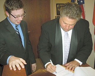 Tom Shay, left, 19, Braceville Township’s new fiscal officer, stands by as Dan Polivka, Trumbull County commissioner, completes the paperwork for Shay’s recent swearing-in ceremony. Shay was elected to a four-year term in November.