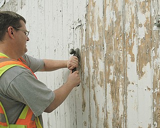 Travis Csuti , 35, of Youngstown, a participant in the day-reporting work program of the Mahoning County Sheriff ’s Office, removes paint and staples from the side of a barn at the Canfield Fairgrounds. He was among
five day-reporting offenders scraping and painting horse barns there Wednesday.