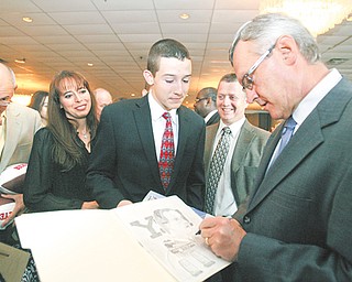 Jim Tressel, former Youngstown State and Ohio State football coach, autographs a drawing for Anthony Lattanzio, 15, of Poland at the United Way’s Champions Among Us dinner Thursday at Mr. Anthony’s in Boardman. Also speaking at the fundraiser was Penn State senior running back Michael Zordich, a graduate of