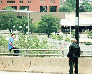 John Sylvester Jr. sits on the Market Street bridge Sunday as a police official talks with him. Sylvester was wanted for a stabbing incident in Boardman earlier in the day and fled to the bridge, where for four hours he kept police at bay with threats to jump before finally surrendering.