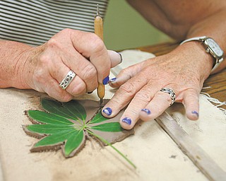 Colleen Boyle of Youngstown cuts out a leaf she has pressed into clay that will be a decoration on her “green man” wall hanging. Boyle was among students who attended a workshop Tuesday at the D.D. and Velma Davis
Education & Visitor Center at Mill Creek MetroParks.
