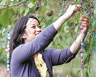Jess Briganti of Youngstown hangs strands of beads from trees at Mill Creek MetroParks’ Fellows Riverside Gardens.