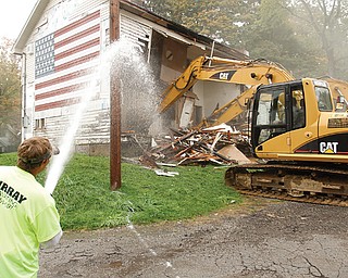 Scott Benbel sprays water to keep down dust as a mechanical shovel demolishes American Legion Post 472 on East Indianola Avenue in Youngstown. If all goes according to plan, a new, one-story ranch-style building will rise at the same location within 60 days to replace the original, which was built in the late 1800s.