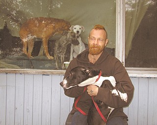 Michael Kelley, one of two people living at 2518 Hamilton St. SW, holds Oreo, one of the four dogs he and his girlfriend, Tiffany Charlton, keep at the home. The three others are shown behind him inside the house. The Warren Police Department and Warren Health Department ordered the house cleaned up and seven of the 11 dogs removed late last month because of conditions.