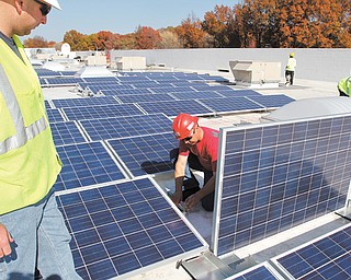 Steve Fife, job foreman from Joe Dickey Electric, works on one of nearly 2,000 solar panels being installed on the roof of the Walmart in Liberty Township as Matt Giles, project manager from The Romanoff Group, looks on.