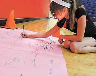 Austintown Middle School students are talking about their families’ struggles with various types of cancer. Here, Devyn Coast signs a paper with the names of people in her family.