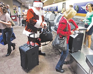 Holiday travelers, including Santa Claus, check in with customer service agent Angelee Arciniega, right, for their Southwest Airlines flight at Sky Harbor International Airport in Phoenix. Thousands passed through the airport, many on their way home for Christmas. This year looks to be a busy holiday travel year, especially on the roads.