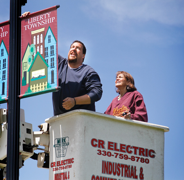 Top, Liberty Trustee Jason Rubin attaches a banner to a lamppost on Shady Road bridge Wednesday. The banners are a finishing touch on a bridge refurbishment project that began three years ago. Above, Rubin and Trustee Jodi Stoyak hoisted eight banners onto four lampposts throughout the day. Stoyak said the banners are meant to boost community pride as well as school spirit.