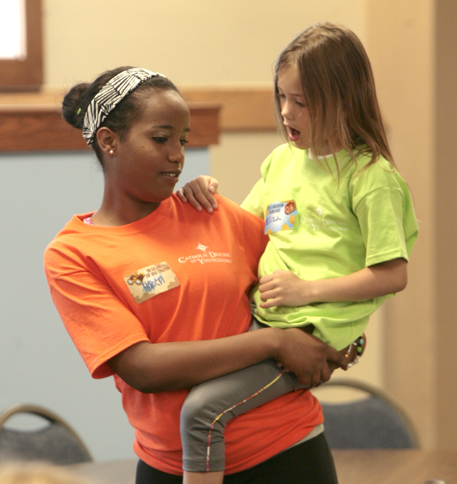        ROBERT K. YOSAY  | THE VINDICATOR

Helping hand  as  Eliza Farr 7 gets a lift from counselor Haben Voorhies as they move from the craft area to the music area
the Downtown Mission’s Children’s Art Camp, currently under way at St. Columba Cathedral parish hall about 25 participants enjoy the activities.
