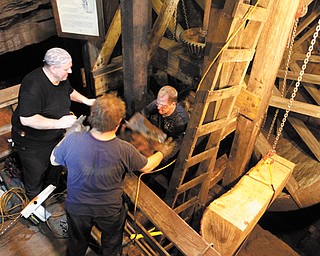 David Siembieda, owner of All-Do-It Technical Services LLC of Youngstown, hands up a piece of a beam being removed from Mill Creek Park’s Lanterman’s Mill to his workers, Gary Kaszowski, in background, and Joe Oates on Tuesday. The new support beam for the water wheel hangs from the chain at right, ready to be installed.