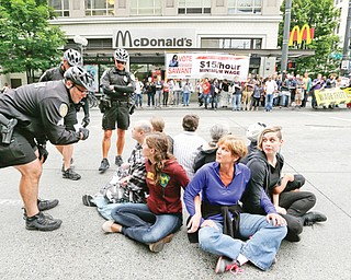 In this photo taken Thursday, a Seattle police officer leans in to explain the arrest procedure to a group of eight protesters blocking a downtown intersection in Seattle. Seattle police said they made several arrests at the demonstration protesting what marchers say are low wages and improper treatment for fast-food workers.