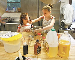 Anna Sherman, 13, stirs ingredients while her 9-year-old sister Hattie watches as the two help their mother, Susan Hura, during a baking session of honey cakes for Rosh Hashanah, which begins at sundown today.
Congregation Ohev Tzedek in Boardman offered the cakes for sale. A Rosh Hashanah tradition is to eat something with honey to ensure a “sweet” new year. Below, pans of baked honey cakes are removed from the oven.