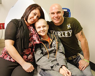 Ty Cook, 14, recovering from brain-cancer surgery and nearly a year of radiation and chemotherapy, sits on an examination table at Akron Children’s Hospital Mahoning Valley with his parents, Angela and Shawn Cook. Ty, a freshman at Struthers High School, was back in the classroom last week for the first time in about a year.
