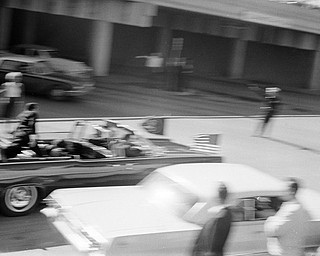 President Kennedy's limousine speeds along Elm Street toward the Stemmons Freeway overpass moments after he was shot at Dealey Plaza in Dallas, Tex., Nov. 22, 1963. Secret Service agent Clint Hill is seen on the back of the car as Jacqueline Kennedy tends to her fatally wounded husband. 