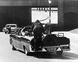 President John F. Kennedy slumps down in the back seat of the Presidential limousine as it speeds along Elm Street toward the Stemmons Freeway overpass after being fatally shot in Dallas on Nov. 22, 1963.  Mrs. Jacqueline Kennedy leans over the president as Secret Service agent Clinton Hill rides on the back of the car.  (AP Photo/Ike Altgens)