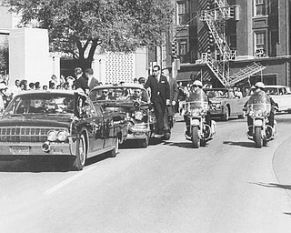 Seen through the limousine's windshield as it proceeds along Elm Street past the Texas School Book Depository, President John F. Kennedy appears to raise his hand toward his head within seconds of being fatally shot in Dallas, Nov 22, 1963. Mrs. Jacqueline Kennedy holds the President's forearm in an effort to aid him. Gov. John Connally of Texas, who was in the front seat, was also shot. (AP Photo/James W. (Ike) Altgens)