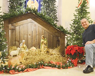 Wes Scott, a member of St. Joseph the Provider Church in Campbell, sets a poinsettia plant next to the manger that is the focal point of the Christmas decorations at the church. He said the manger has a “rough look” to mimic a stable.