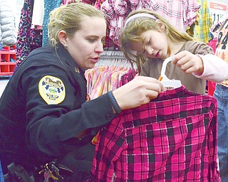 Capt. Stacy Karis of the Lowellville Police Department helps Reese Agee, 5, of Poland pick out a shirt during the Shop with a Cop program at Walmart in Boardman on Sunday. About 90 children in need took part in
the event, in which they were accompanied by police officers and firefighters, mostly from Struthers and Lowellville, to shop for clothes, toys and other items. “It’s all about giving back to the community,” Karis said.