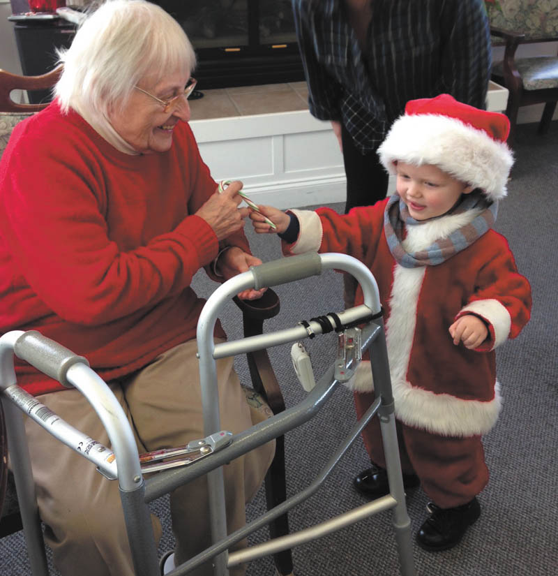 SPECIAL TO THE VINDICATOR: Paxton Gabbert, 3,  Santa’s little helper, spread Christmas cheer recently to the residents of Whispering Pines Village in Columbiana. Above is resident Martha Bell, enjoying his company and pleased by his gift of a candy cane. Whispering Pines is an assisted-living and independent-living facility at 937 E. Park Ave. 