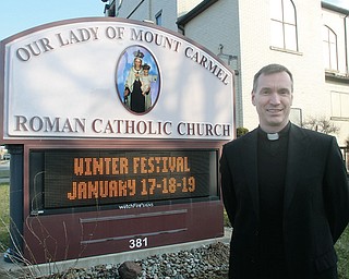 The Rev. John-Michael Lavelle, pastor of Our Lady of Mount Carmel Church, Niles, stands next to a sign promoting the winter festival this weekend. The church’s summer festival, a tradition for more than 80 years, inspired the January event to satisfy those summer food cravings.
