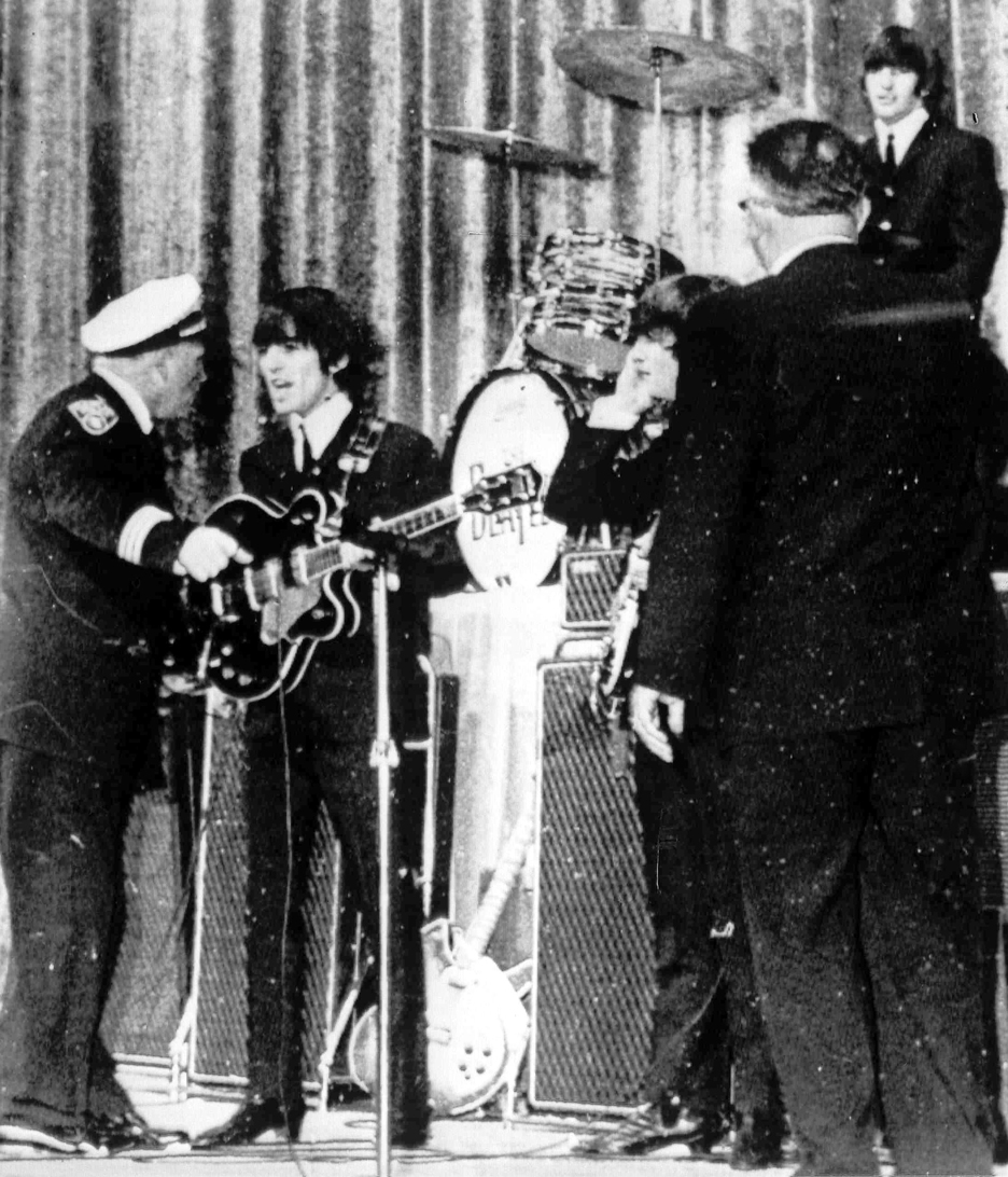 Police Inspector Carl Bear of Cleveland's Juvenile Bureau, left, orders George Harrison and the other members of the British pop group The Beatles, off the stage of the Public hall, Cleveland, Ohio, Sept. 16, 1964 as teenagers rushed the stage. Bear let the group back on ater wailing youngsters were given 15 minutes to cool down. From left to right, Bear, Harrison, John Lennon, unknown, and Ringo Starr, top right. (AP Photo)